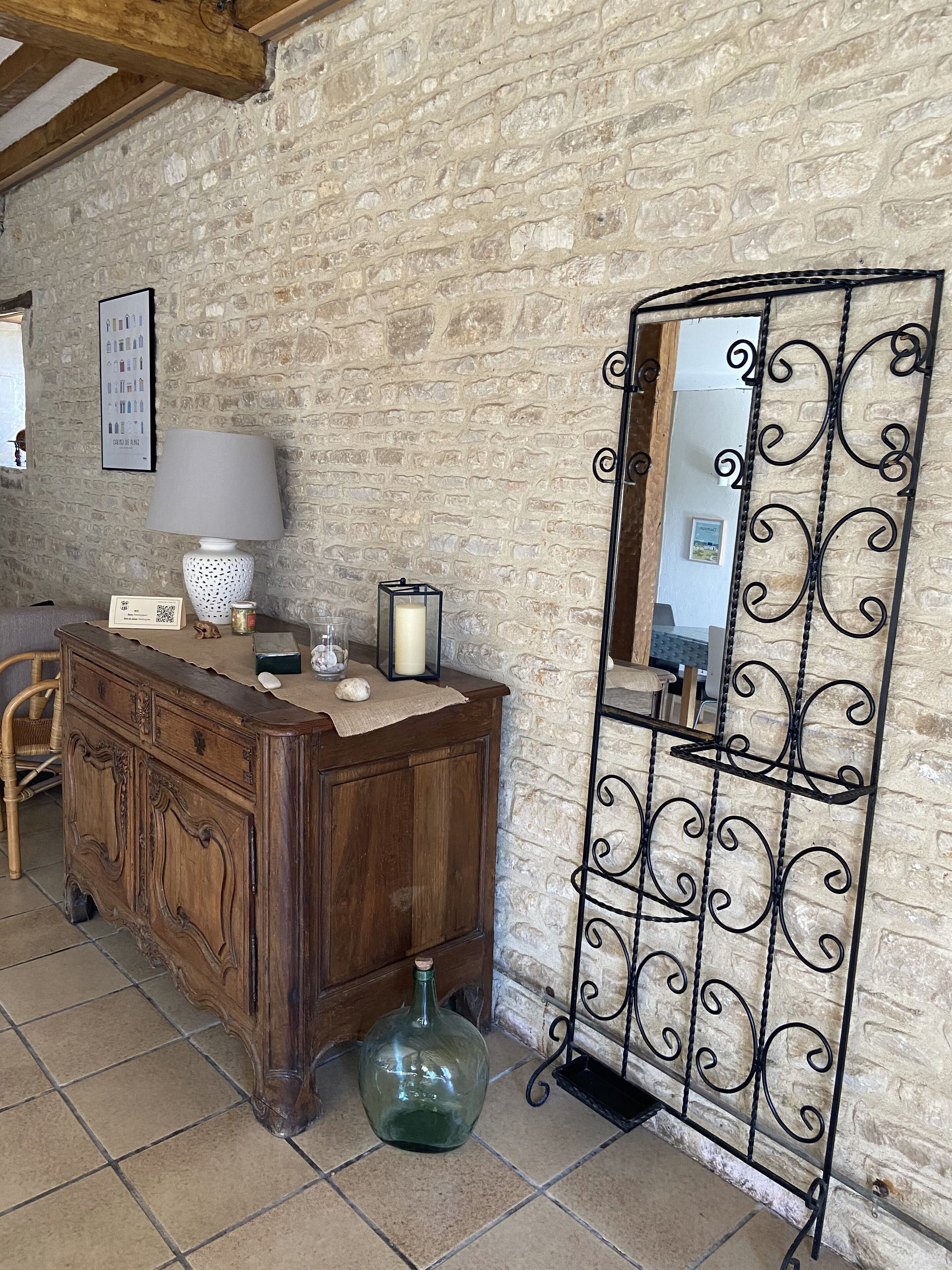A rustic room with a wooden dresser, a mirror with decorative metal frame, and a stone wall.
