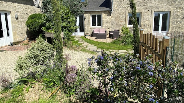Una casa de piedra con un patio, mobiliario exterior y un jardín con diversas plantas y flores.