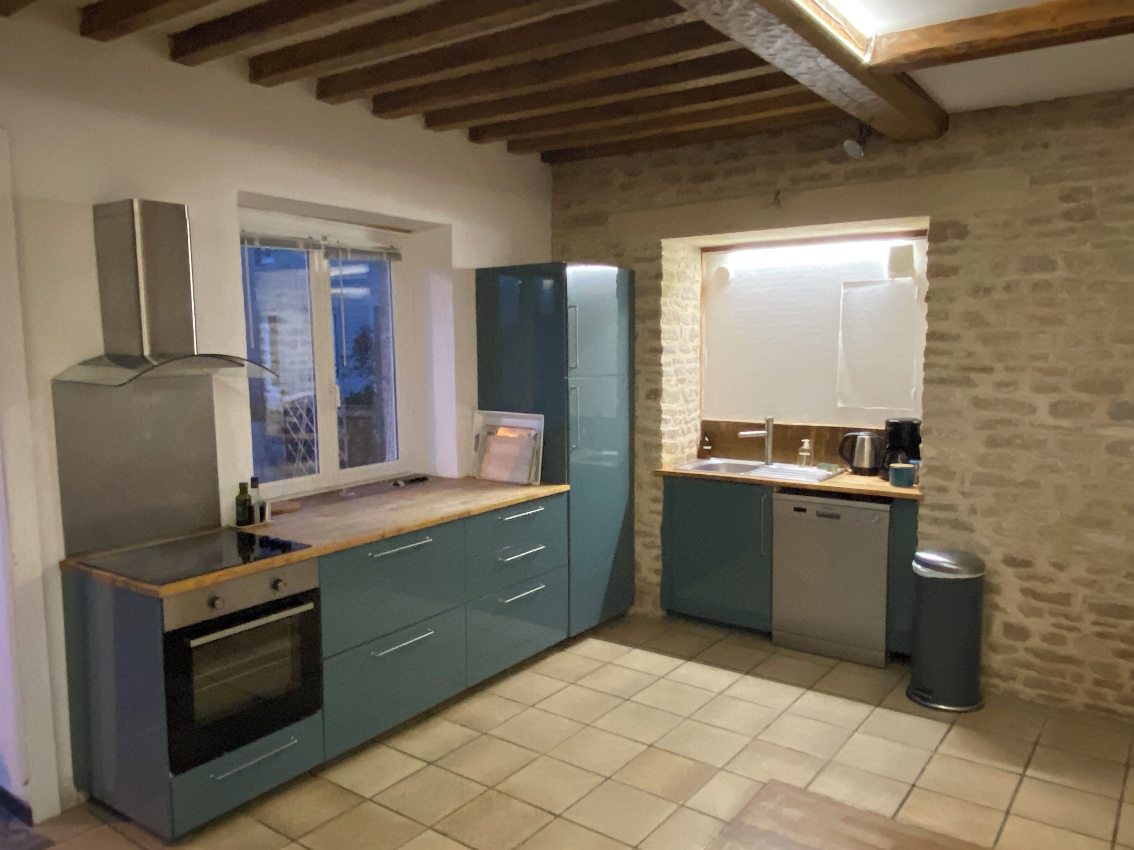 Une cuisine compacte dotée d’un four encastré, d’une fenêtre et d’un mur en pierre.