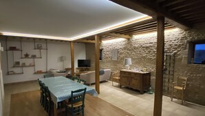 Un comedor con una mesa, sillas, televisor y una pared de piedra.