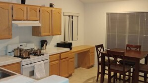 A compact kitchen with wooden cabinets, a stove, and a dining area with a table and chairs. - Pet-Friendly Vegas House w/ EV Charger & Parking (Las Vegas)