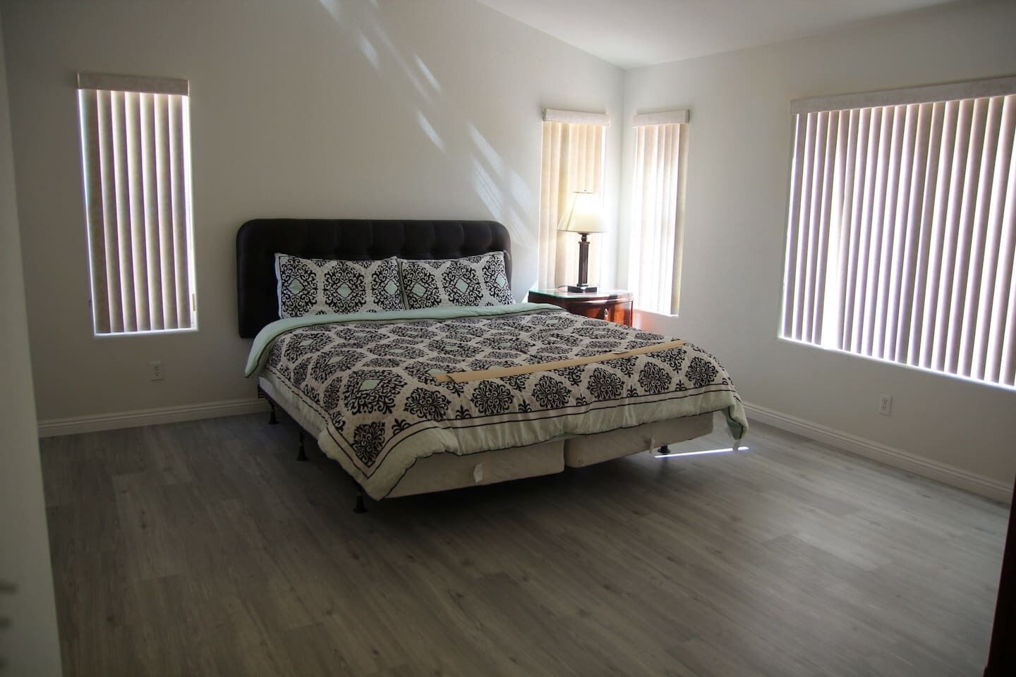 A bedroom with a bed, two bedside tables, and three windows with blinds.