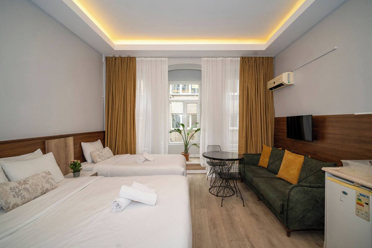 A hotel room with two beds, a sofa, a small table, and a TV.