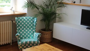 A living room with a polka-dotted armchair, a wooden coffee table, a potted plant, a radiator, and a television on a white cabinet.