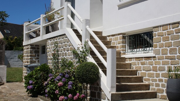 A two-story house with a stone facade, white exterior, and a set of white stairs leading to the entrance.
