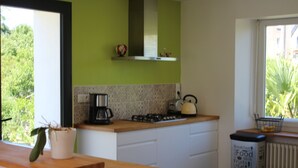 A kitchen with a wooden countertop, a gas stove, a kettle, and a trash bin.