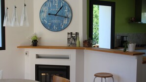 A modern kitchen with a blue clock, pendant lights, a wooden countertop, and a view of greenery outside.