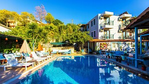 A swimming pool with lounge chairs and umbrellas, surrounded by buildings and greenery. - Tuthaliya Hotel (Kas)