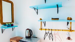 A compact room with a small kitchenette, wooden flooring, a mirror, and wall-mounted shelves with various items. - Tuthaliya Hotel (Kas)