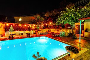 Una piscina con sillones de descanso y sombrillas, rodeada por un muro de piedra y árboles.
