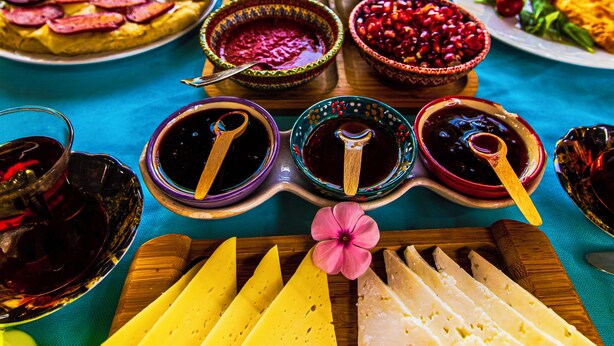 A table with various food items and condiments, including a pizza, cheese, and bowls of fruit and sauces. - Tuthaliya Hotel (Kas)
