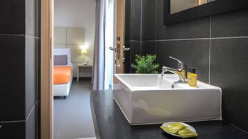 A modern bathroom with a white sink, dark tiled walls, a small potted plant, and a bottle of lotion on the counter.