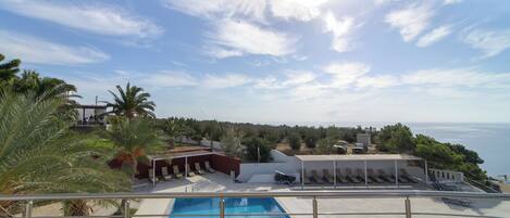 Zona de piscina con vista al mar, sillas de descanso y un área de estar cubierta.
