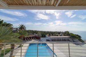 Zona de piscina con vista al mar, sillas de descanso y un área de estar cubierta.