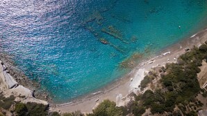 Vue aérienne d’une plage aux eaux turquoise et limpides, bordée de formations rocheuses et d’une végétation clairsemée.