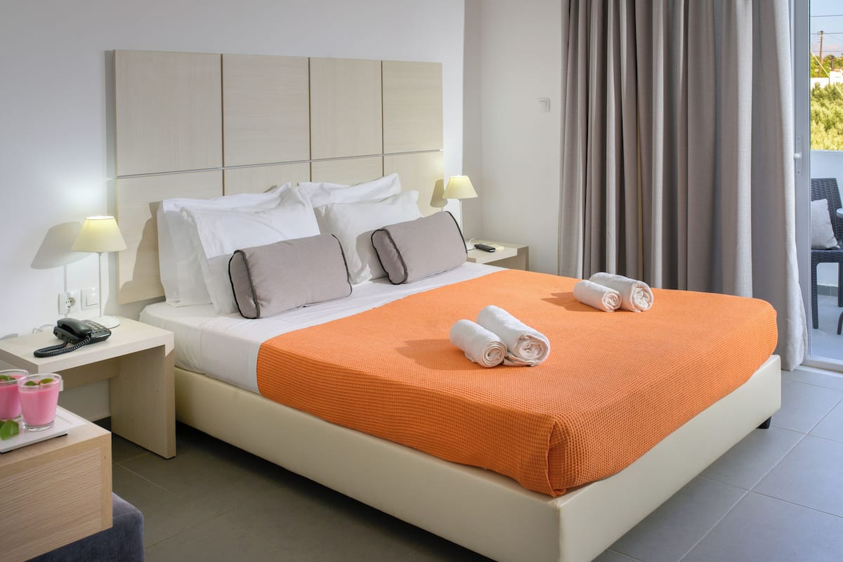 Une chambre d’hôtel avec un grand lit, deux tables de chevet, une commode, une lampe et une vue sur l’extérieur.