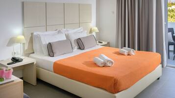 A hotel room with a large bed, two bedside tables, a nightstand, a lamp, and a view of the outdoors.