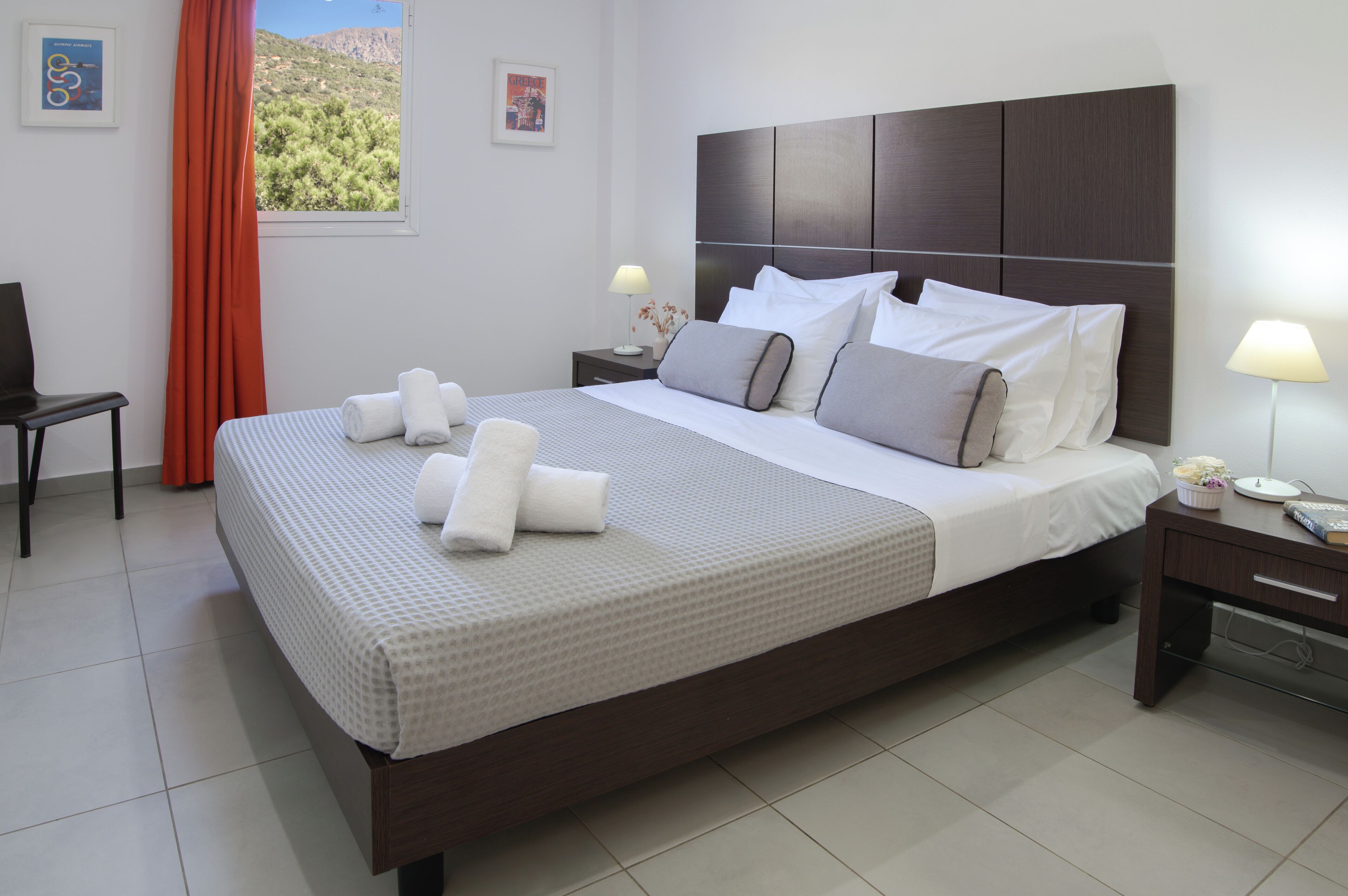 A neatly made bed with white and gray linens, a wooden headboard, and two bedside tables with lamps.
