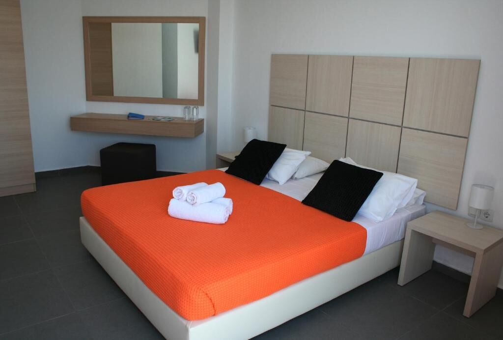 A hotel room with a large bed, a bedside table, a mirror, and a small stool.
