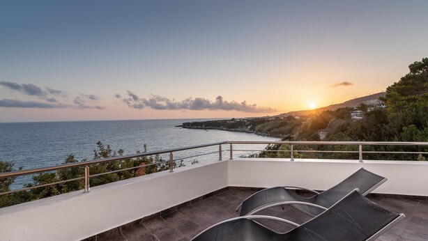 Un balcon avec deux fauteuils confortables donnant sur une vue de la côte au coucher du soleil.