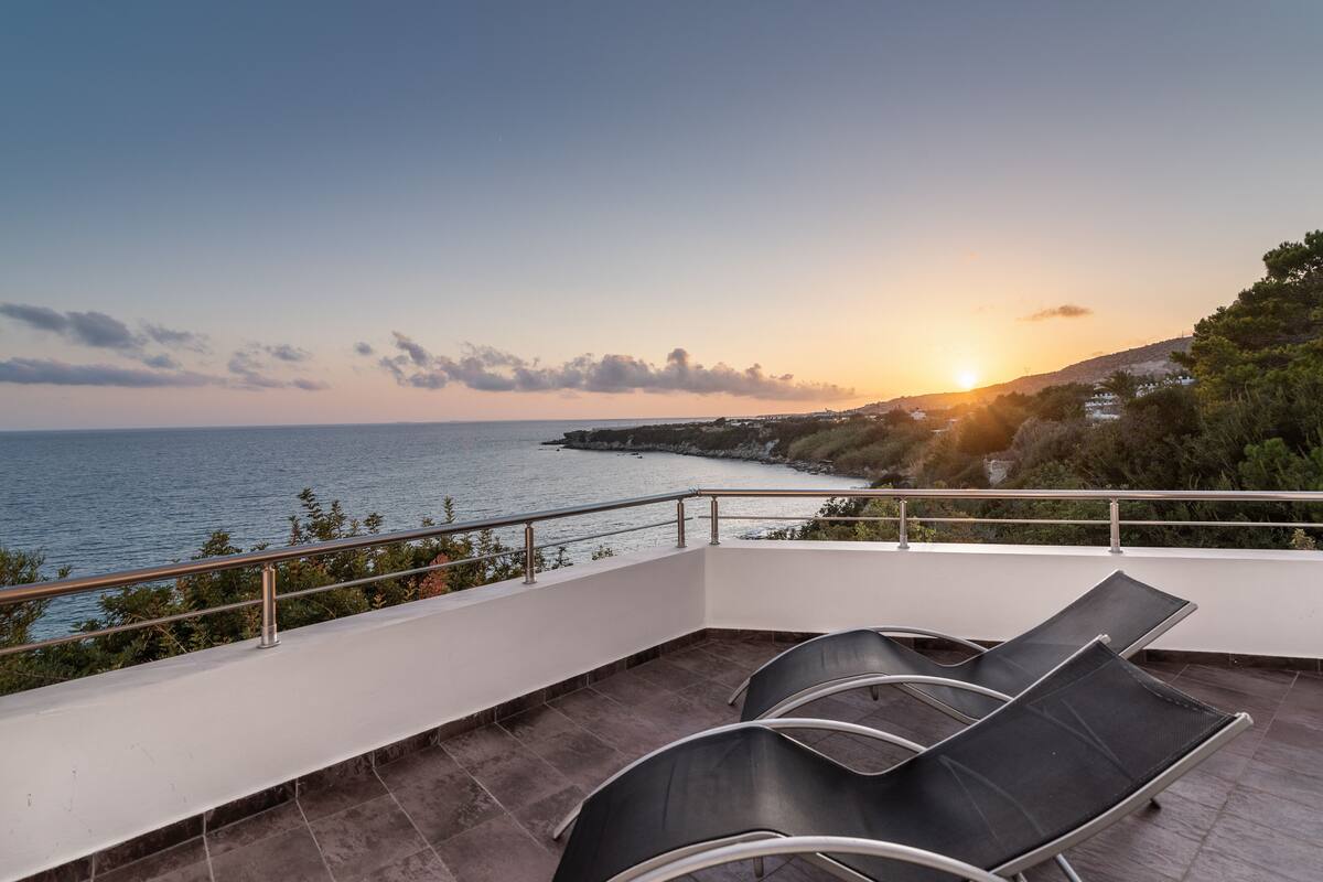 Un balcon avec deux fauteuils confortables donnant sur une vue de la côte au coucher du soleil.