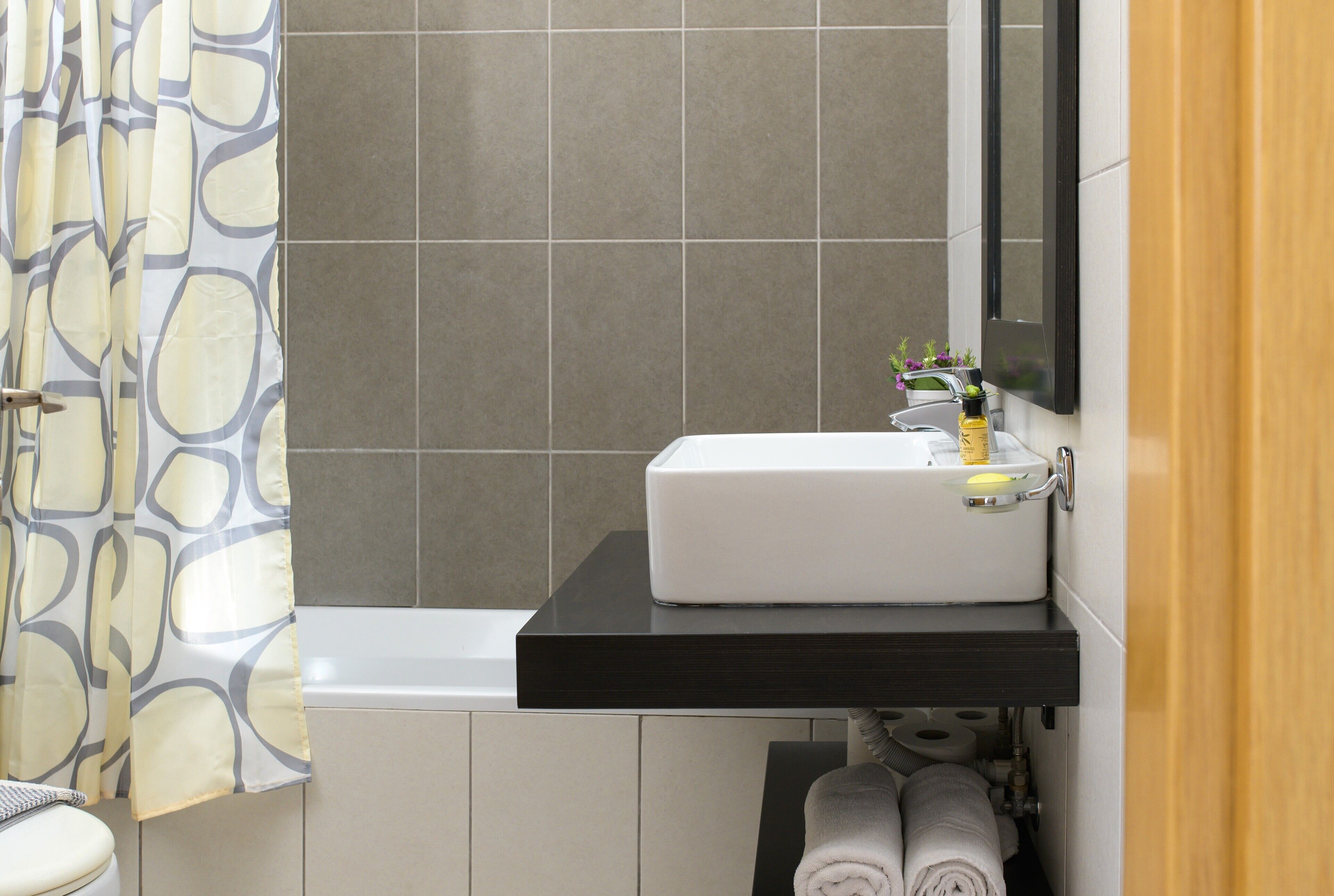 Une salle de bain avec un lavabo blanc, un plan de toilette noir, un miroir et un porte-serviettes.