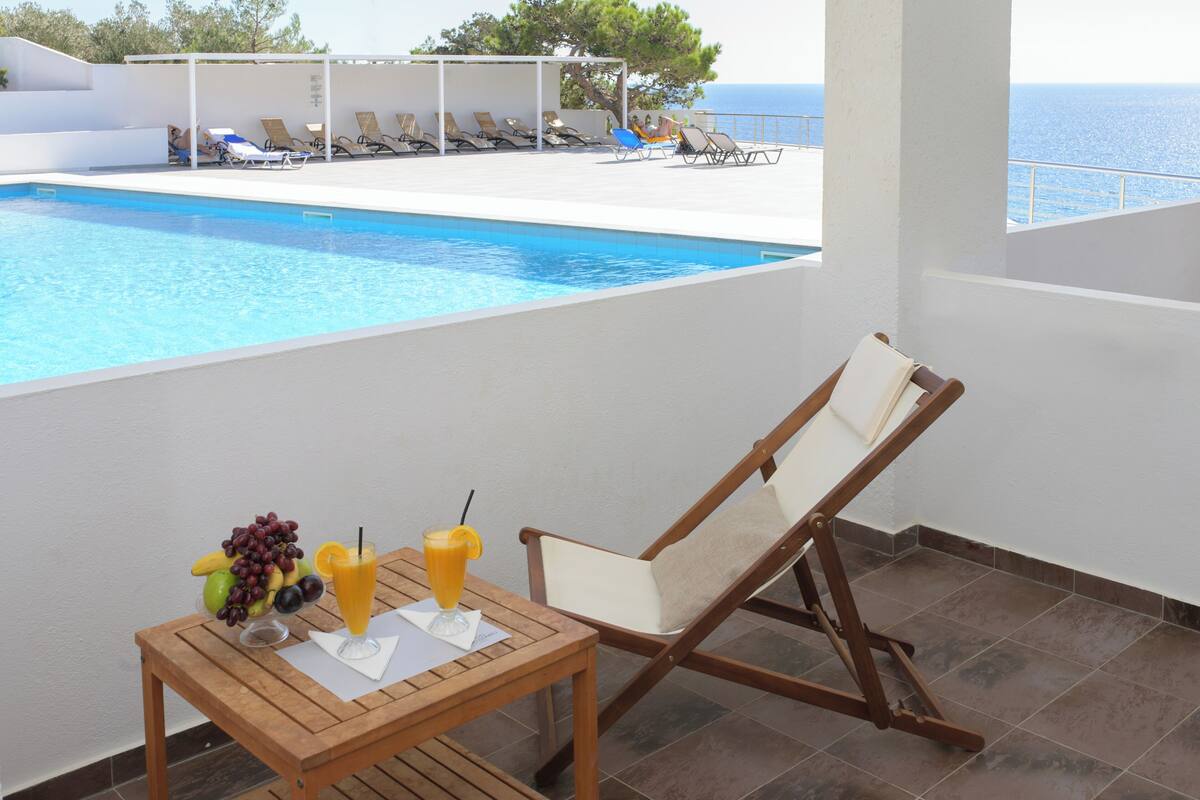 Un espace aménagé au bord de la piscine, avec une table dressée où l’on trouve des fruits et des boissons, des chaises longues et une vue sur la mer.