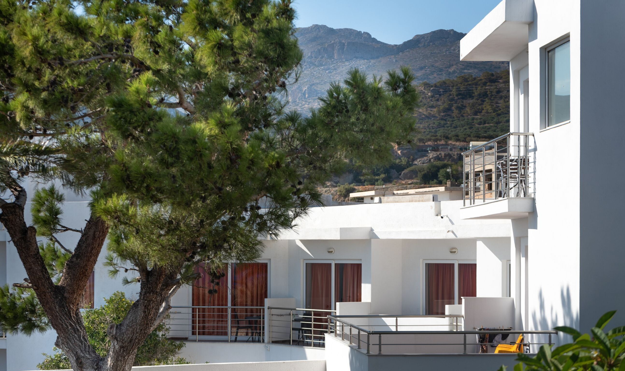 A modern building with a balcony, a tree in the foreground, and mountains in the background.