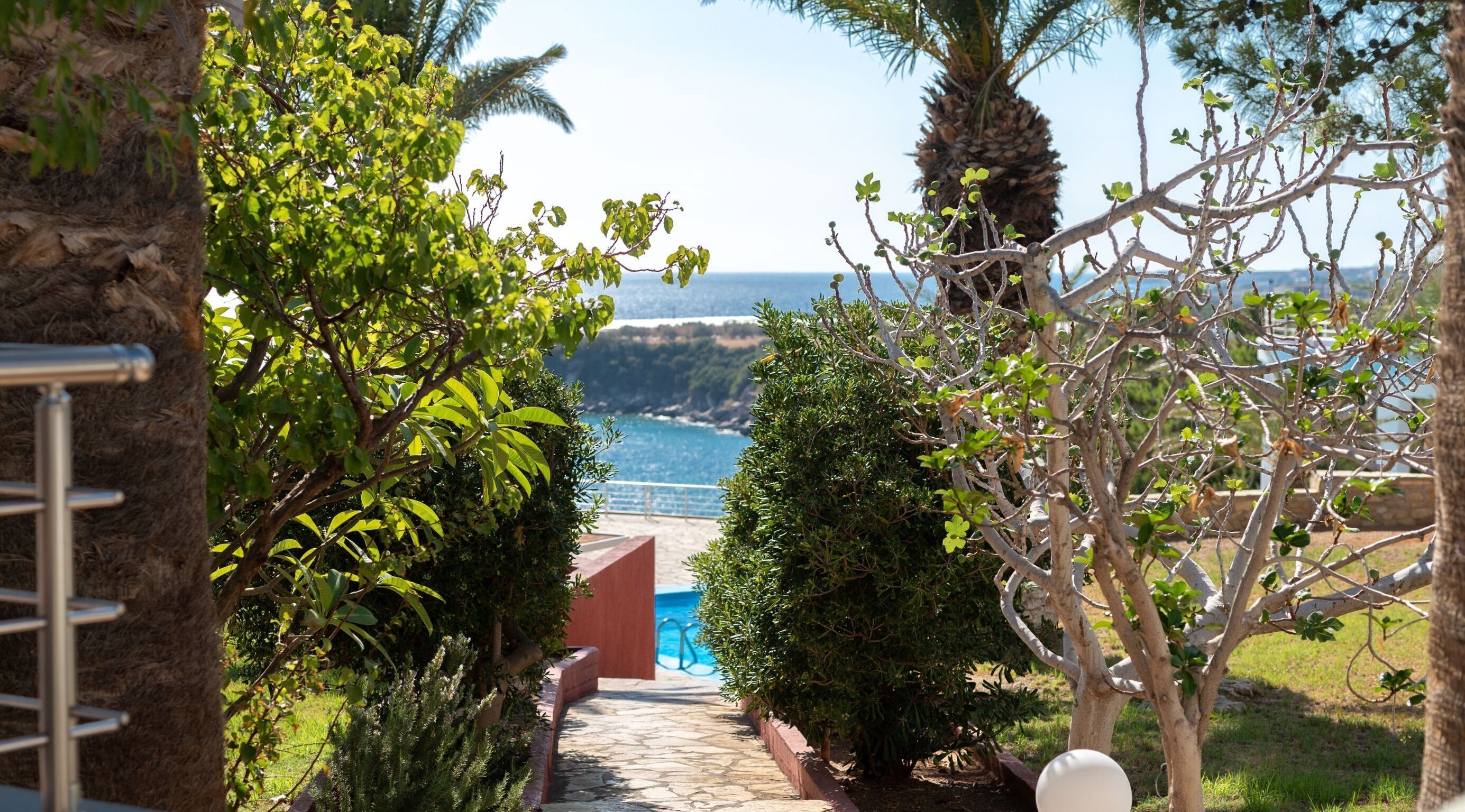 A pathway leading to a pool with a view of the sea and hills.