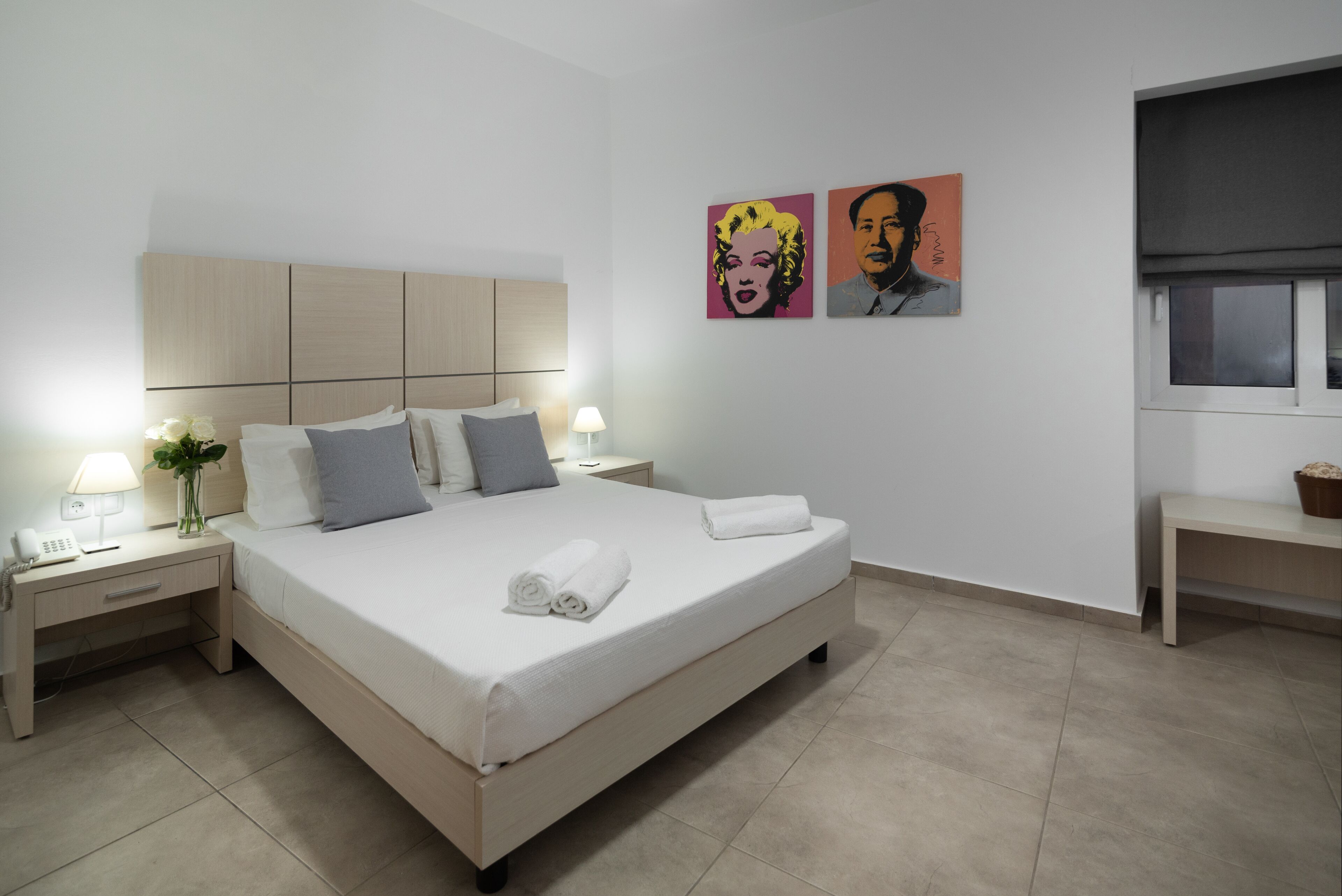 A neatly made bed with a white comforter and pillows, a bedside table with a lamp, and a wall with two framed artworks.