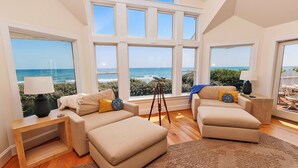 A spacious living room with large windows offering ocean views, a cozy sofa, a wooden side table, and a tripod with a telescope. - OCEANFRONT, Ocean views, ELEV, Private Pool, Private beach access, WL1083, Lighthouse Drive (Corolla)