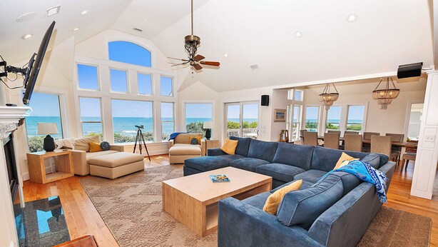 A spacious living room with a large sectional sofa, a coffee table, and a fireplace. There are multiple windows offering a view of the ocean. - OCEANFRONT, Ocean views, ELEV, Private Pool, Private beach access, WL1083, Lighthouse Drive (Corolla)