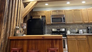 Una cocina rústica con vigas de madera, un refrigerador negro, electrodomésticos de acero inoxidable y taburetes de bar de madera.