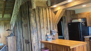 Una cocina rústica con paredes de madera, una barra de madera con taburetes y un refrigerador negro.