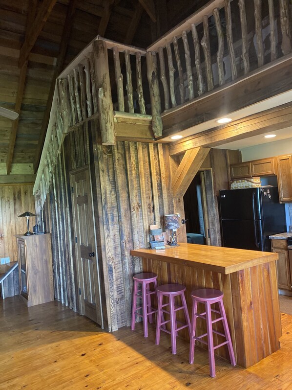 A rustic kitchen with wooden walls, a wooden bar with stools, and a black refrigerator.