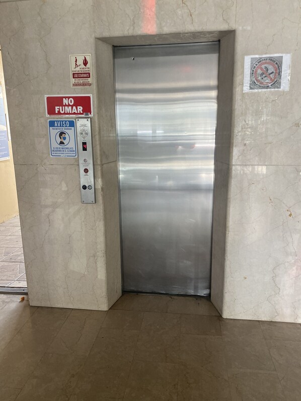 An elevator with a metallic finish, surrounded by safety and security signs, including a no-smoking sign and a mask requirement notice. - Sea Rentals at Dalia 15 (Carolina)