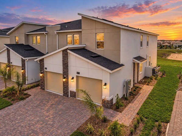 A modern two-story residential building with a brick driveway, a well-maintained lawn, and a clear sky. - Reunion Resort Condo: Waterpark, Clubhouses and fun! (Four Corners)