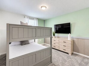 Ein Etagenbett mit Fernseher darüber, eine Kommode mit Schubladen und ein Fenster mit Vorhängen.