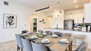 Een moderne keuken met een centraal eiland, roestvrijstalen apparatuur en een eetgedeelte met grijze stoelen en een tafel gedekt voor vier personen.