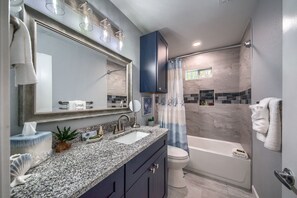 A modern bathroom with a granite countertop, a double sink, a large mirror, and a shower area with a curtain. - Castle Shadow DT 534 3 Bedroom Home by RedAwning (New Braunfels)