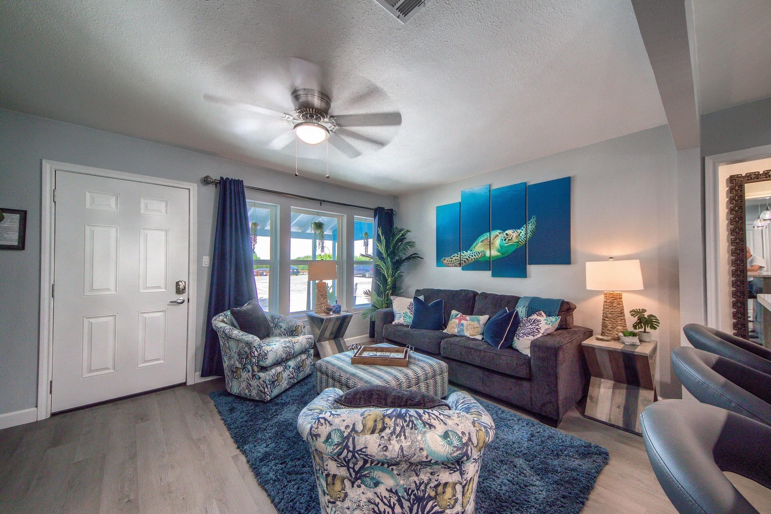 A living room with a ceiling fan, a couch, two armchairs, a coffee table, and a rug.