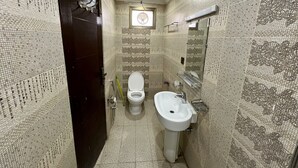 A narrow bathroom with a toilet, sink, and mirror. The walls are tiled with a patterned design. - Khan Continental Hotel & Restaurant (Mansehra)