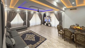 A modern living room with a sofa, a dining table with chairs, a TV, and a patterned rug. - Khan Continental Hotel & Restaurant (Mansehra)