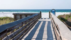 Ein hölzerner Steg führt zum Strand, mit einem Sicherheitsschild.