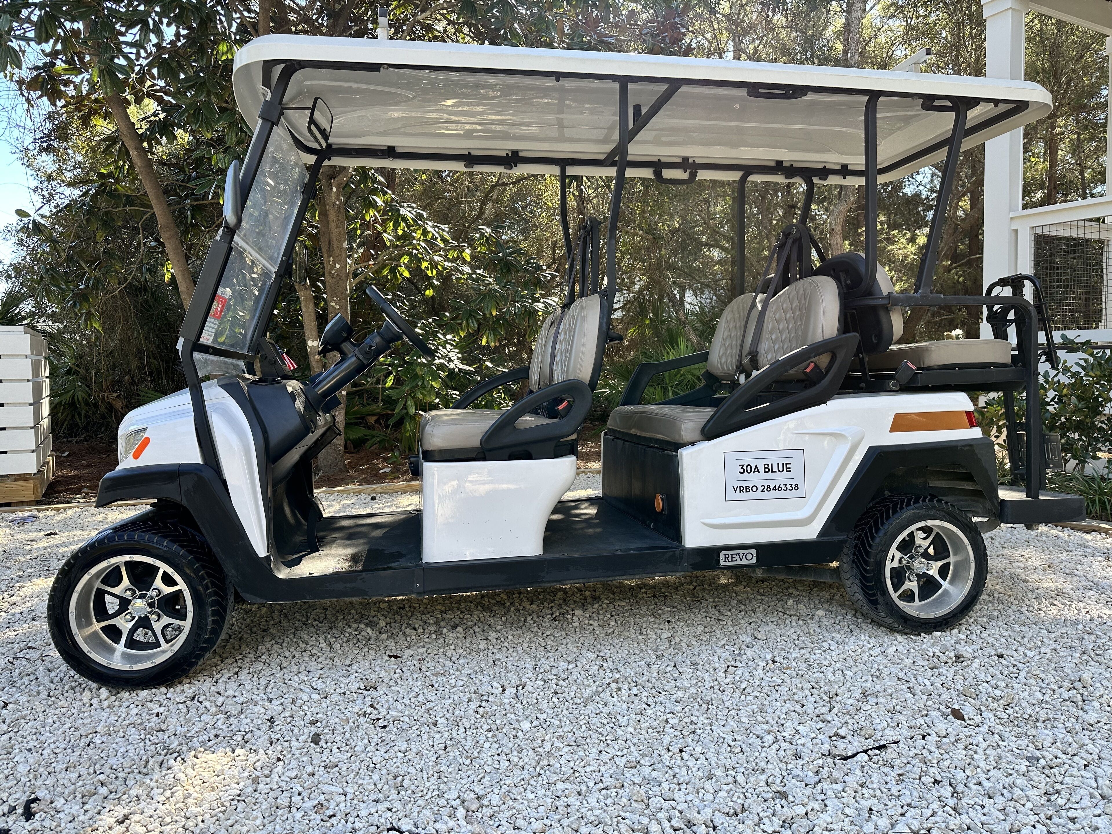 A golf cart with a canopy, labeled '30A BLUE VRBO 2846338', parked on gravel.