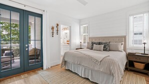 Ein Schlafzimmer mit Bett, Nachttischen, Fenster mit Jalousien, Deckenventilator und einer Tür zu einem Außenbereich.