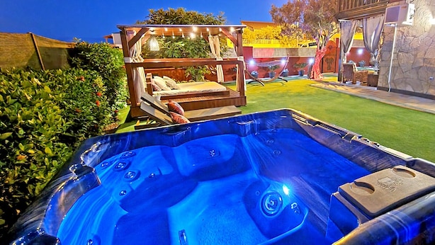 A hot tub with a wooden deck and lounge chairs, surrounded by a well-maintained lawn and a stone wall. - Casa Balimar - Pool, Jacuzzi, Internet, Garten, Meerblick (Tarajalejo)