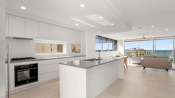 A modern kitchen with white cabinetry, a central island, and a view of the ocean. - Kings Surf Unit 6, 5 Ormonde Tce, Kings Beach (Kings Beach)