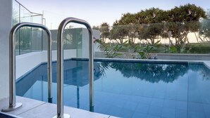 A swimming pool with metal ladders, surrounded by glass walls and a view of trees and a road. - Kings Surf Unit 6, 5 Ormonde Tce, Kings Beach (Kings Beach)