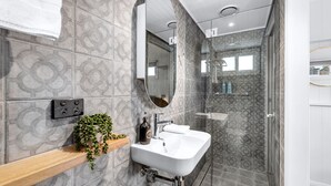 Un baño moderno con baldosas estampadas, un lavamanos blanco, un espejo, cabina de ducha y una planta en un estante.